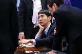 Lee Se-Dol looks up at a man in a suit as he holds his finger on a Go game board