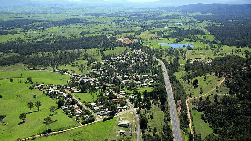 An aerial picture of a small regional town, with a river nearby, surrounded by grassland and trees.