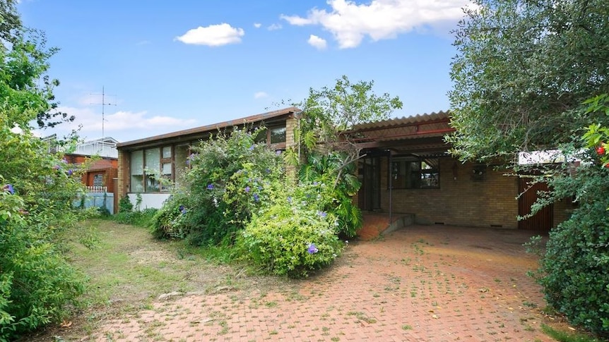 The rundown exterior of a brick home with a flat roof.