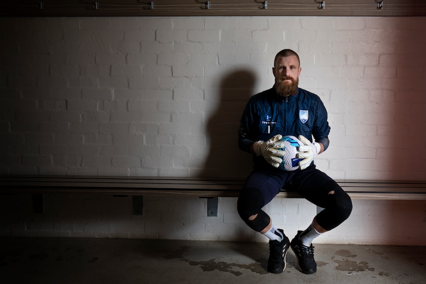 A man with a beard sitting on a bench holding a soccer ball