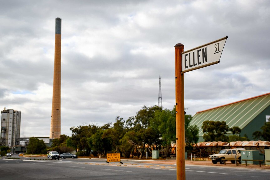 The sign for Ellen Street in the foreground with a large smoke stack from the lead smelter in the background