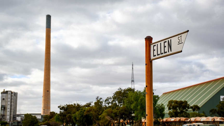 The sign for Ellen Street in the foreground with a large smoke stack from the lead smelter in the background