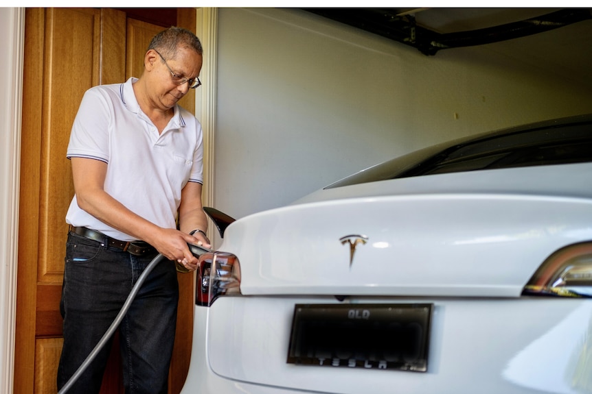 a man standing in a garage charging his electric vehicle
