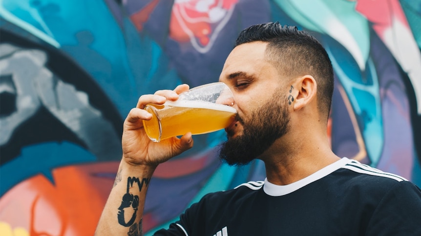 A man in a black t-shirt drinks a beer from a glass