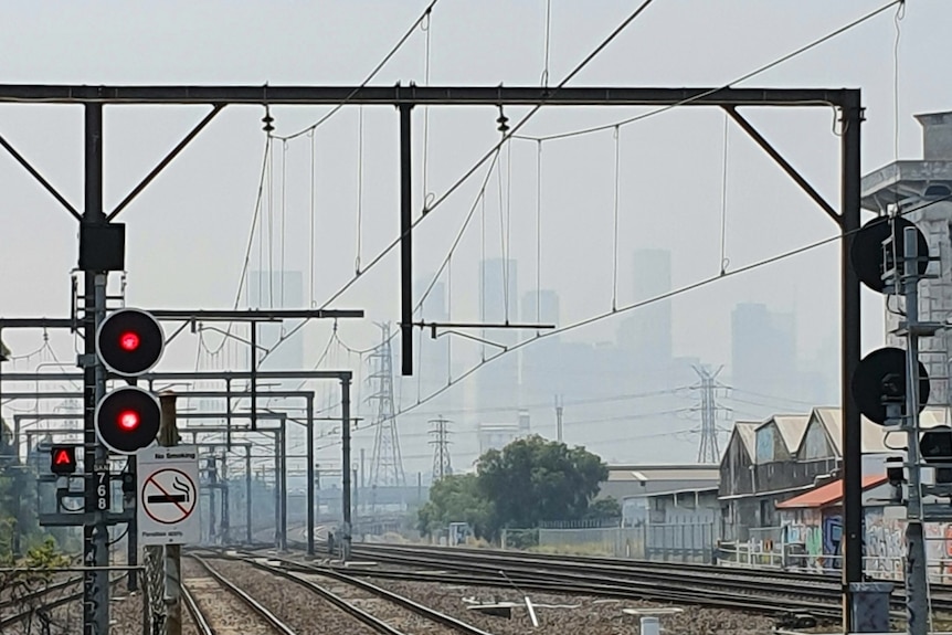 A picture of high rise buildings covered in smoke, with a train line in the front of the picture.