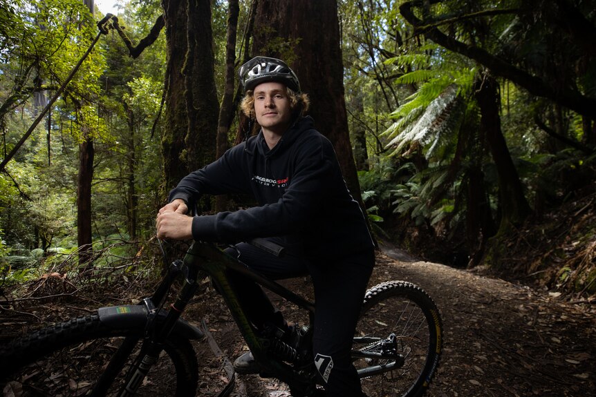 A mountain biker leans on his bike in the middle of a forest.