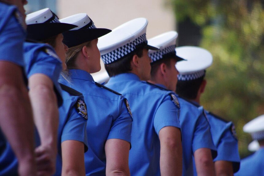Police recruits march in uniform with their backs turned.