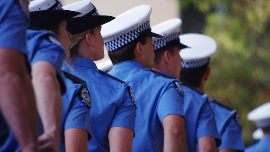 Police recruits march in uniform with their backs turned.