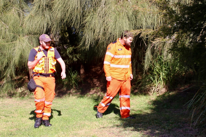 Two men wearing bright orange jumpsuits searching bushland
