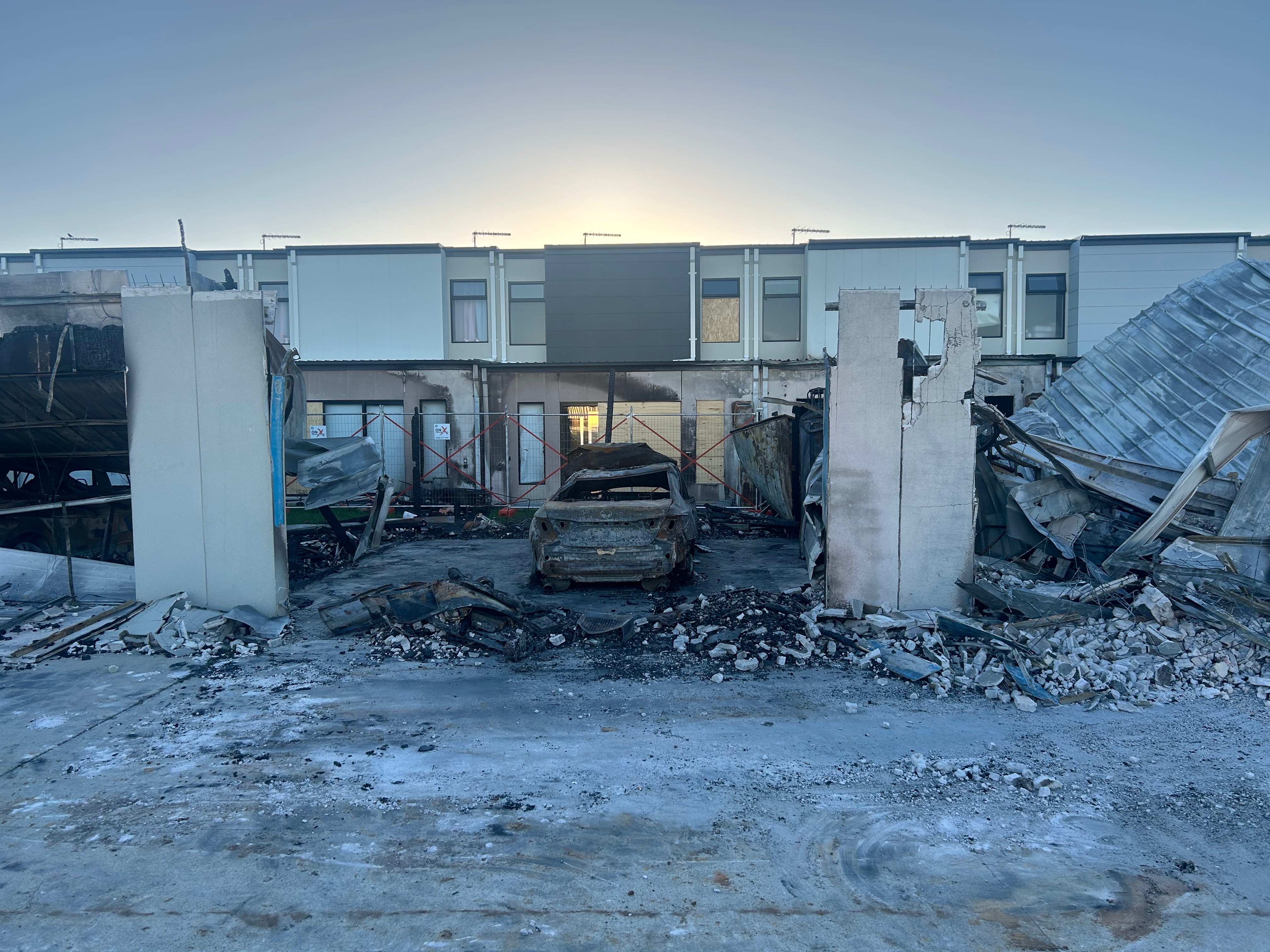a burnt car and charred rubble from collapsed building near apartment block