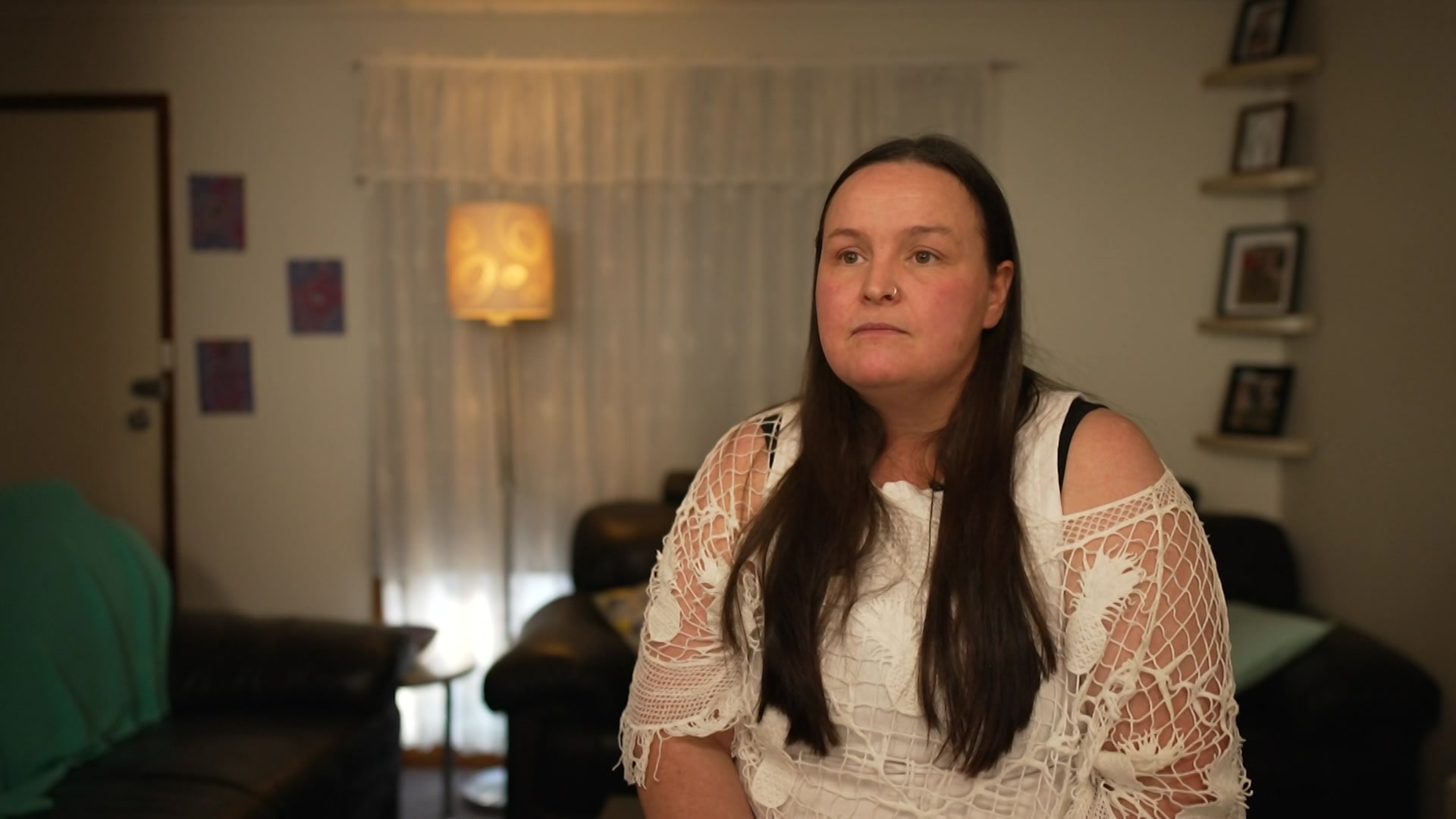 A living room with a seated person, surrounded by furniture, framed photos and a shiny lamp in the area.