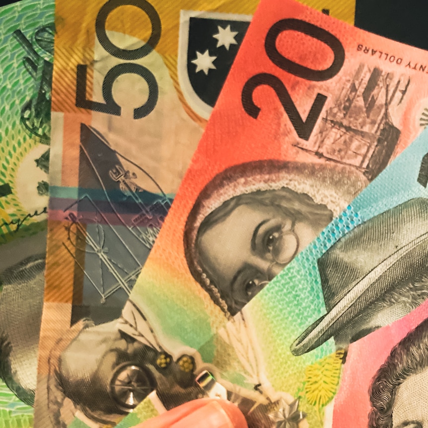 A hand holds various denominations of Australian banknotes.