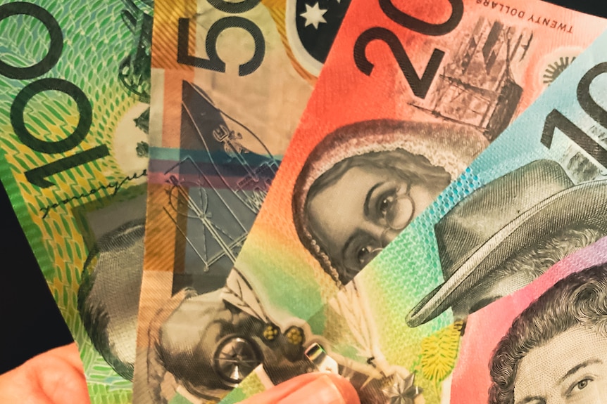 A hand holds various denominations of Australian banknotes.