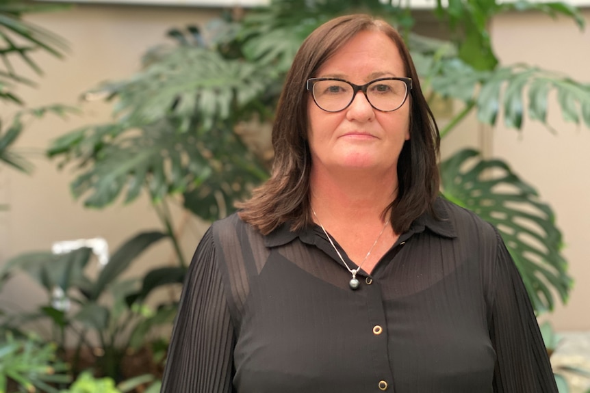 A woman with brown hair and glasses looks serious.