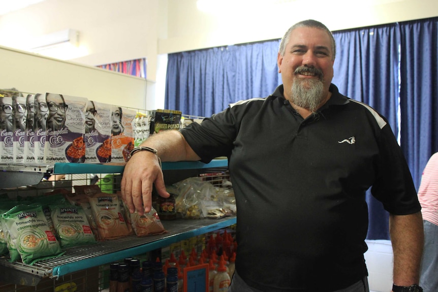 A smiling middle-aged man leans against a supermarket shelf.