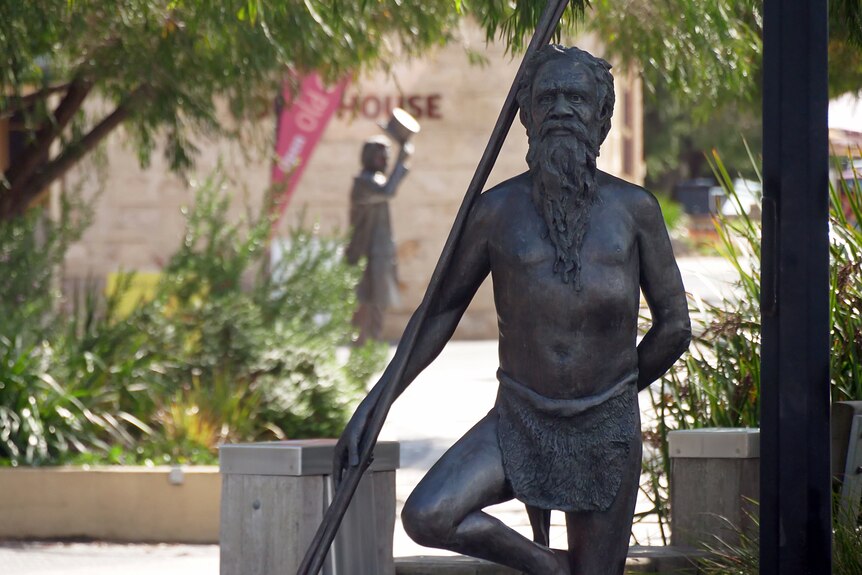 A bronze statue of an Indigenous man with a spear