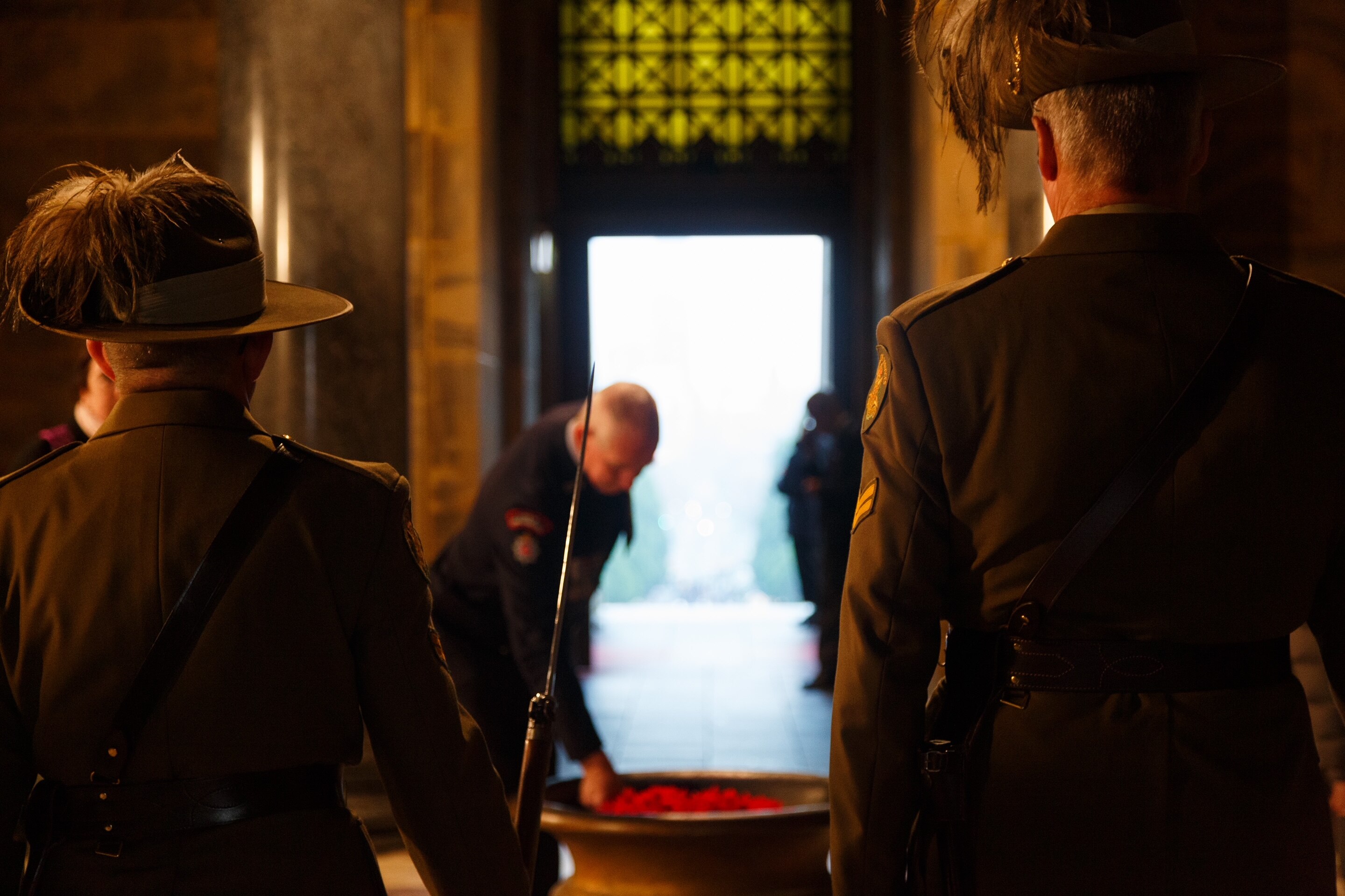 Two men in army uniform watch on as a man in air force uniform lays poppies on a stone tablet.