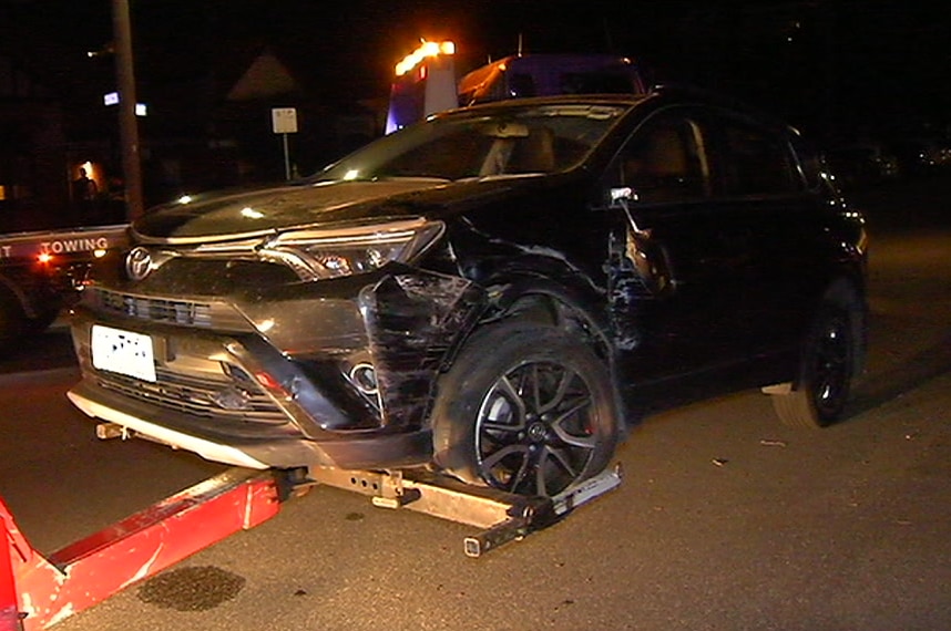 A black SUV with a smashed front bumper being towed away at night.