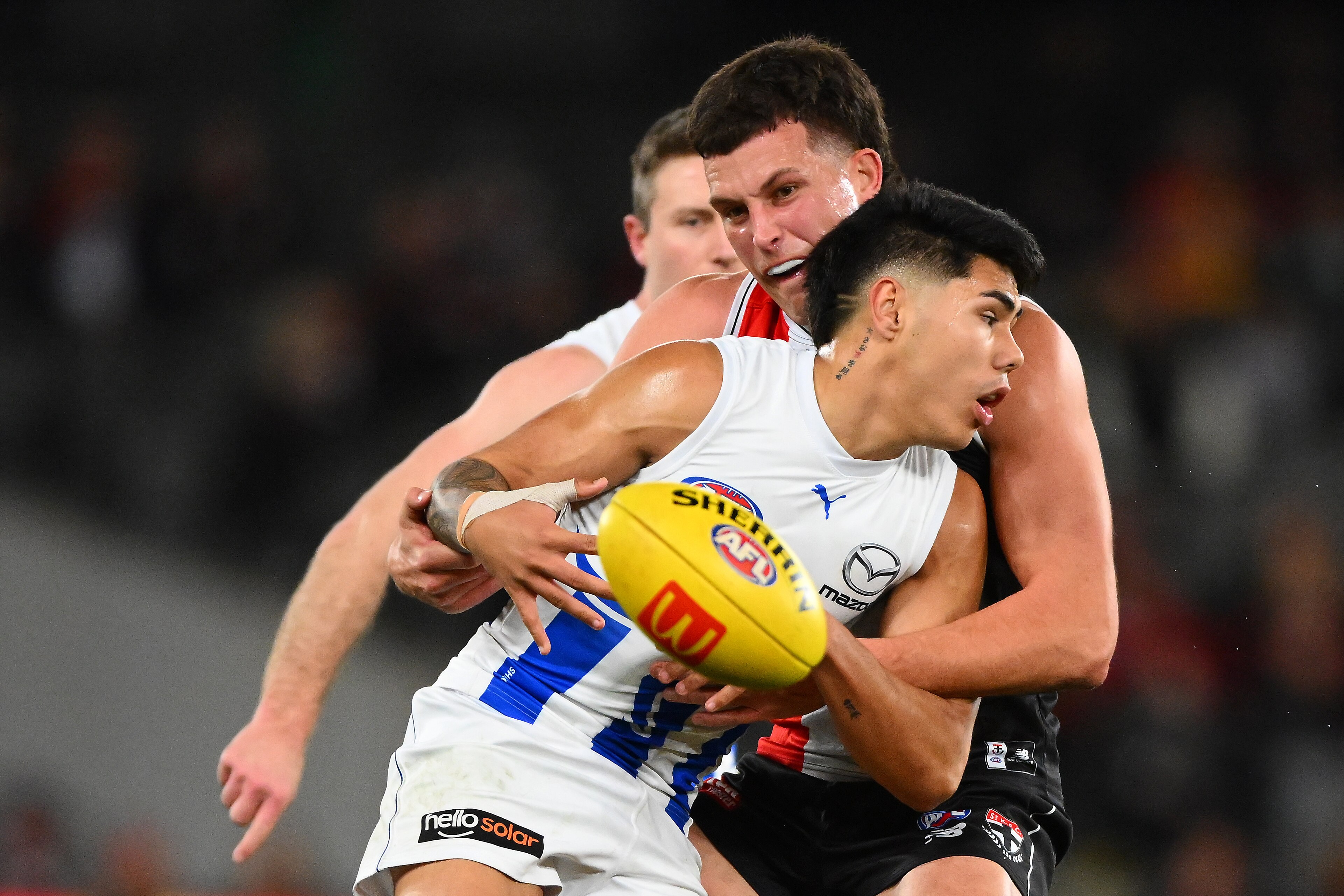 A North Melbourne AFL players holds the ball while being tackled by a St Kilda opponent.