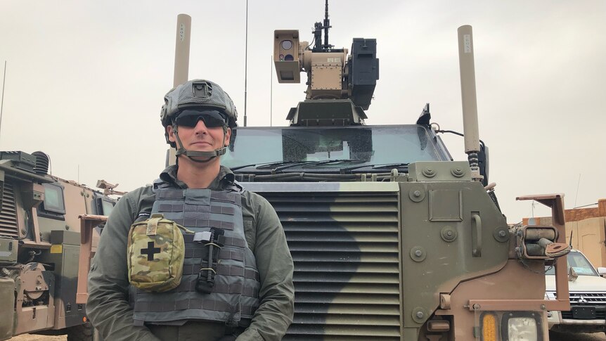 man in a helmet and flak jacket standing in front of a tank