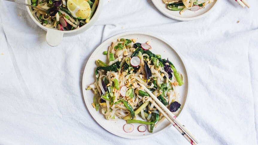 A bowl of pad thai salad with tongs served onto two dinner plates with chopsticks, illustrating our simple recipe.