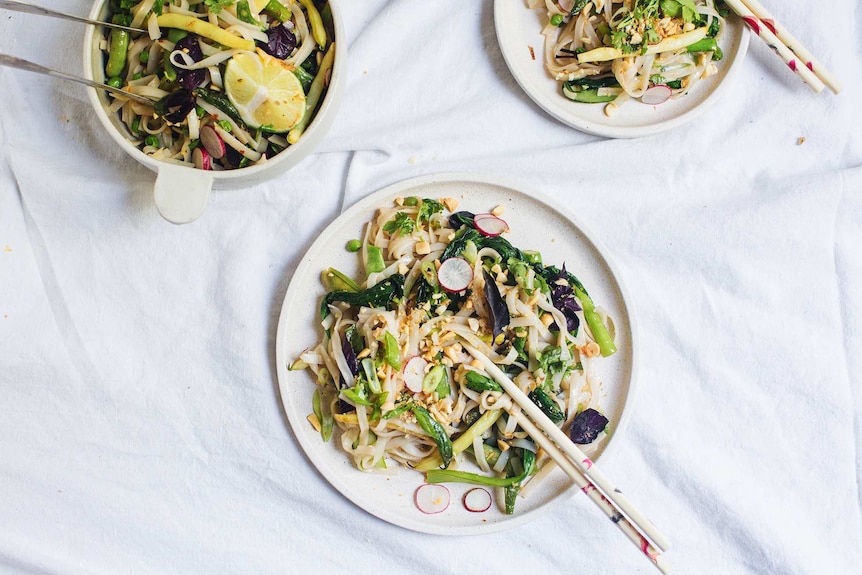 A bowl of pad thai salad with tongs served onto two dinner plates with chopsticks, illustrating our simple recipe.