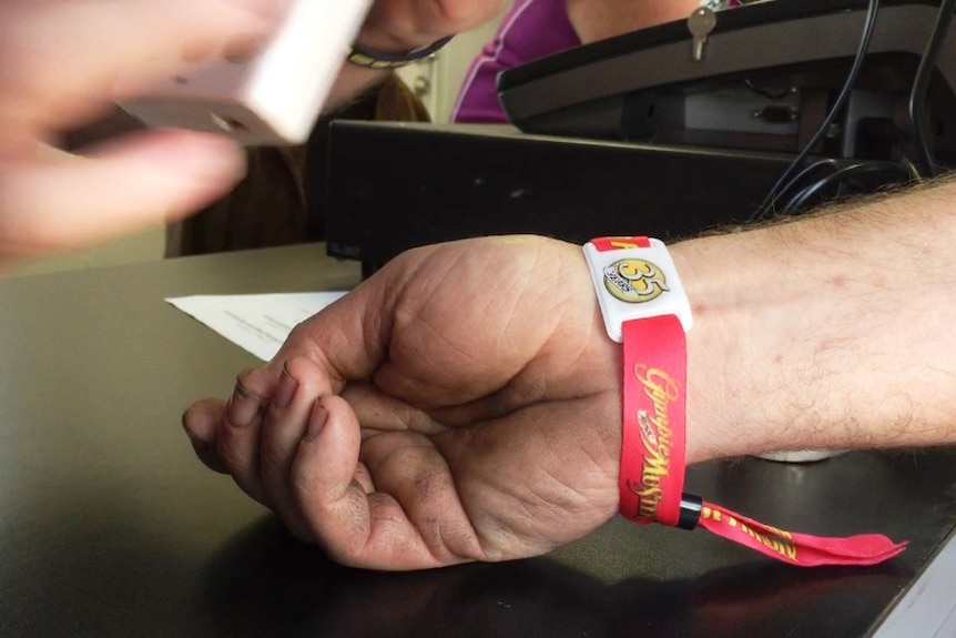 a man's wrist with armband and a yellow 'disc' on the armband which is the chip for scanning.