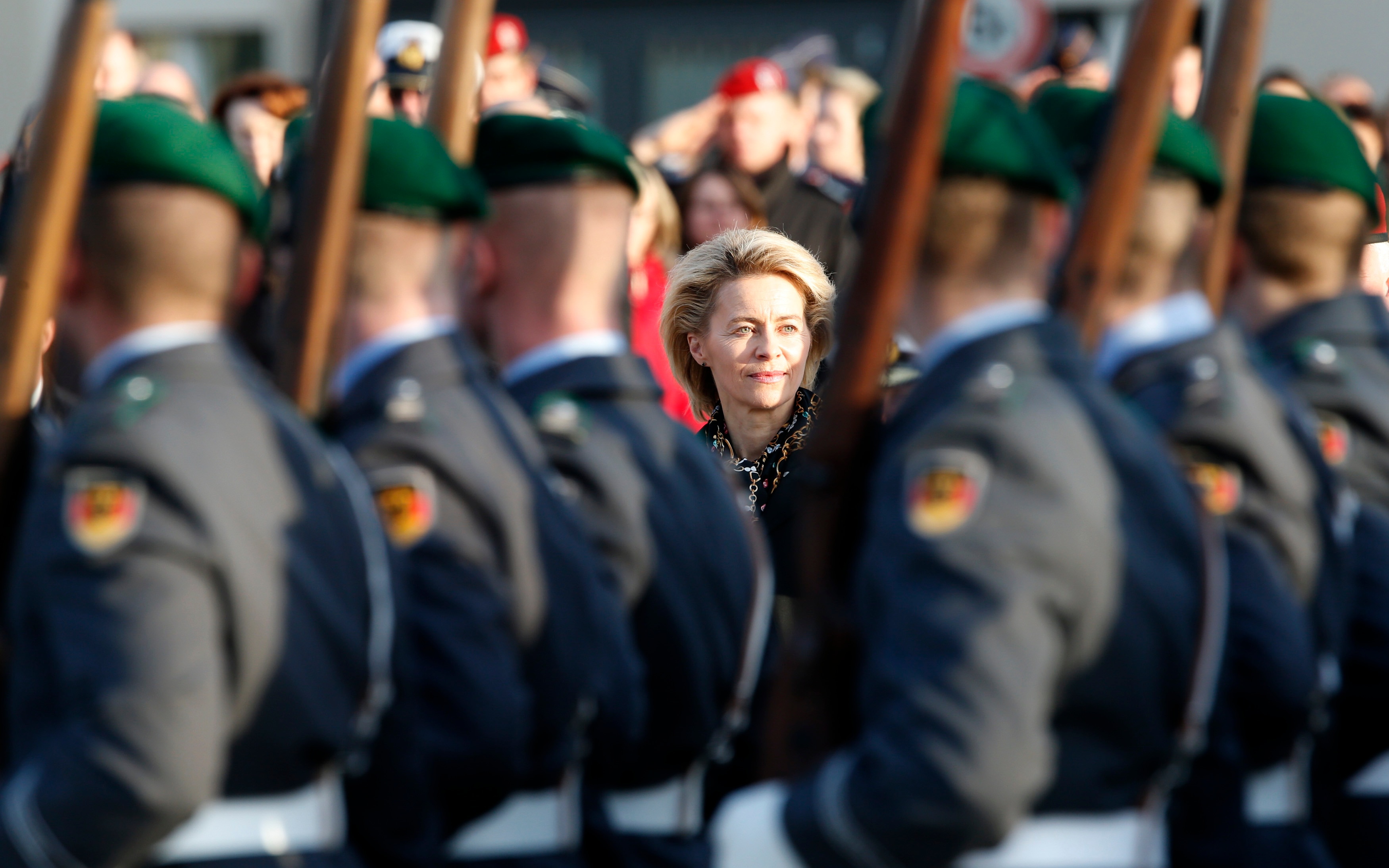 Merkel can be seen in focus in between soldiers who have their backs to the camera who are holding guns over their shoulder