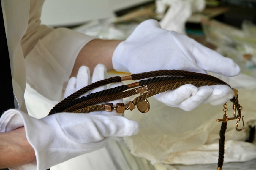 White-gloved hands holding chains made from human hair, used by men to carry watches and accessories