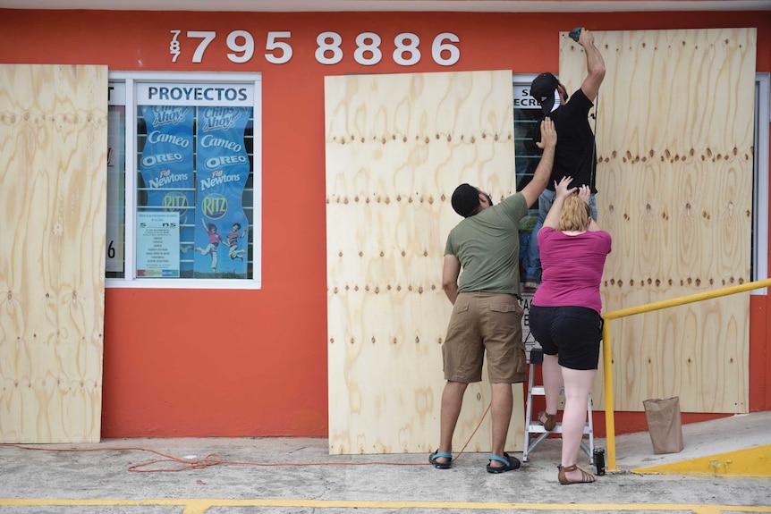 Three people work together to install a wood panel over a shop window.