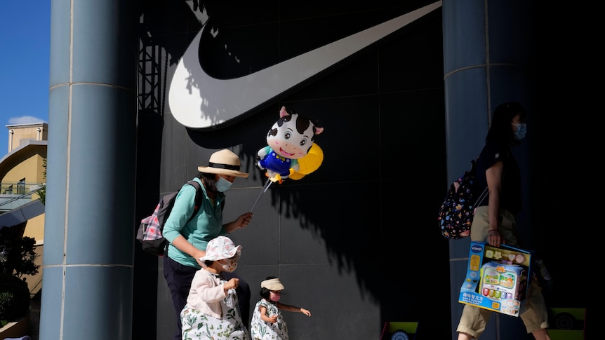 A woman and children wearing masks pass by Nike store in Beijing.
