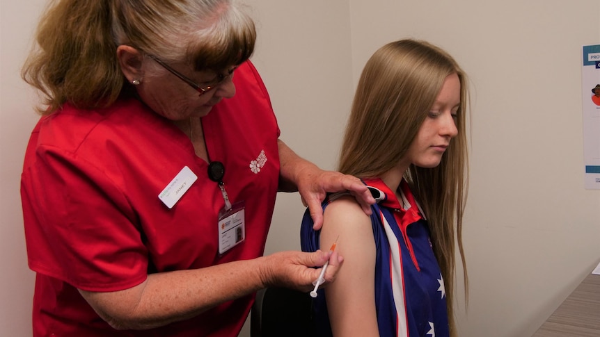 A young girl receives a COVID-19 vaccination in Katherine from a nurse in a red shirt