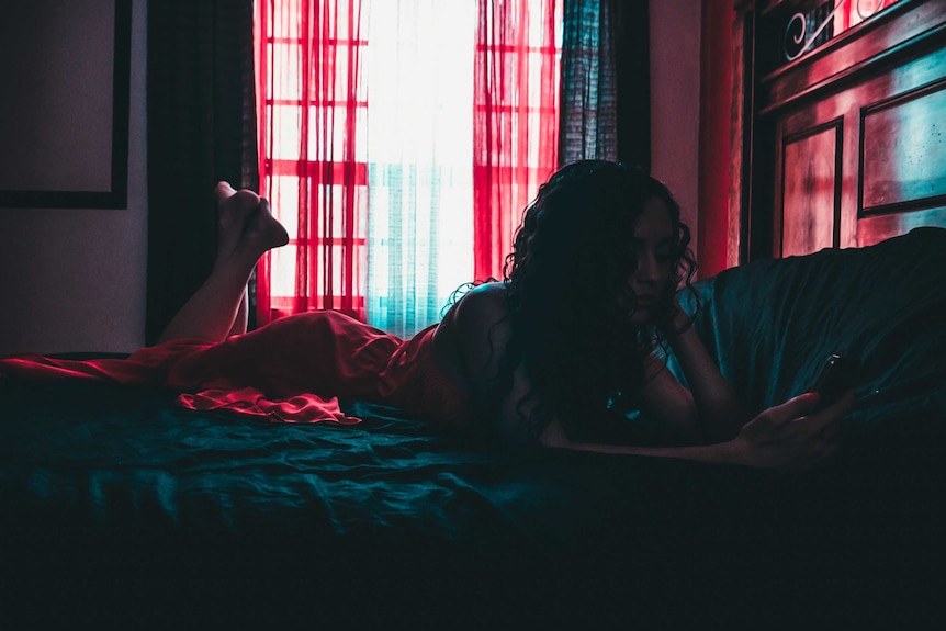 A woman lying in bed looks at a smartphone for a story about online harassment and abuse.
