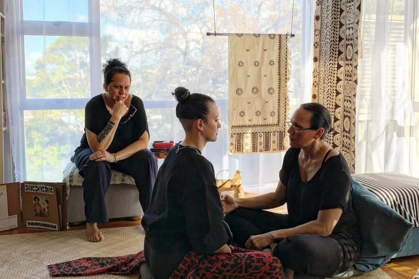 Three women sit in a room with traditional artwork
