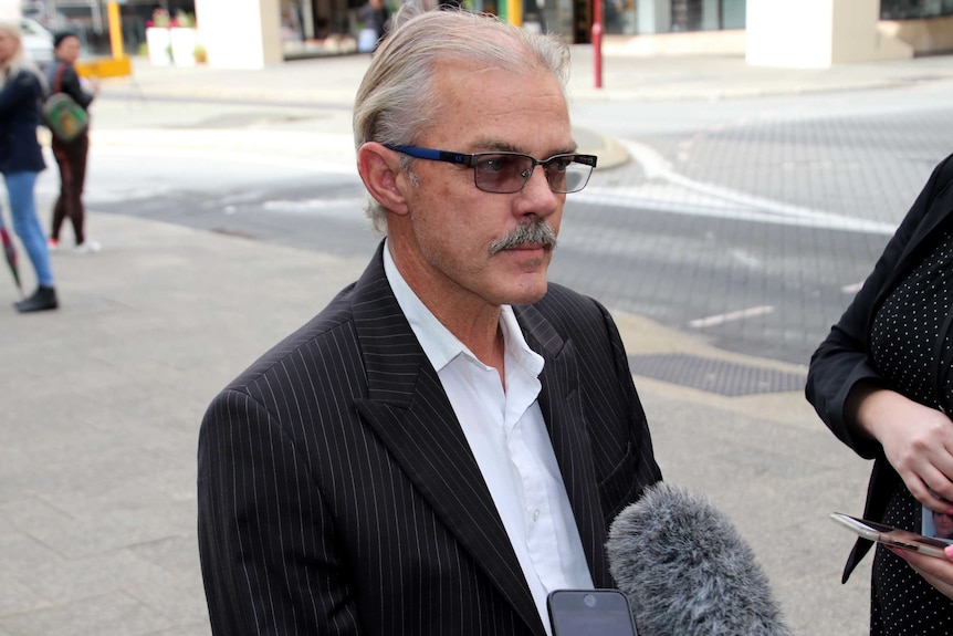 headshot of man with microphones held up to him.