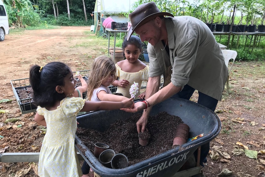 Three little girls and a man stand around a wheelbarrow.