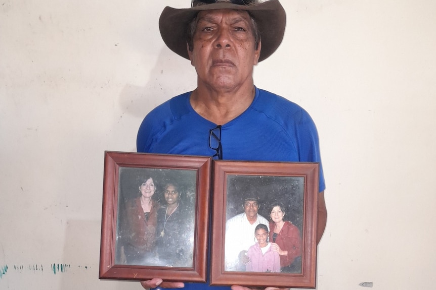 Peter standing with a blue shirt on and brown hat holding two brown photo frames of himself and his daughter with slim dusty