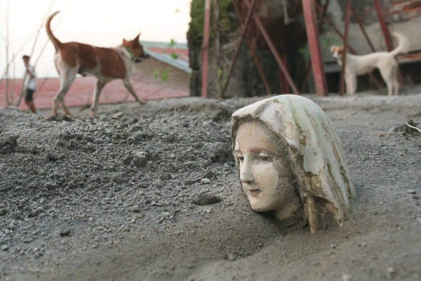 The head of a religious statue with its head above mounds of volcanic ash.