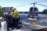 A man prepares chemicals next to a helicopter.