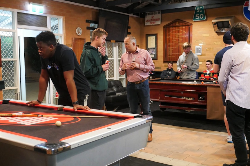 Students talking at a couple of pool tables, with one older man in earnest discussion