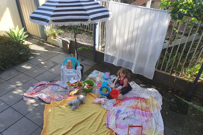 A little girl having a tea party with her toys outside.