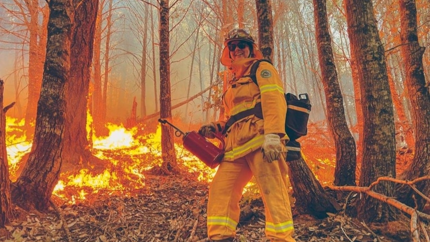 A woman stands in front of a fire