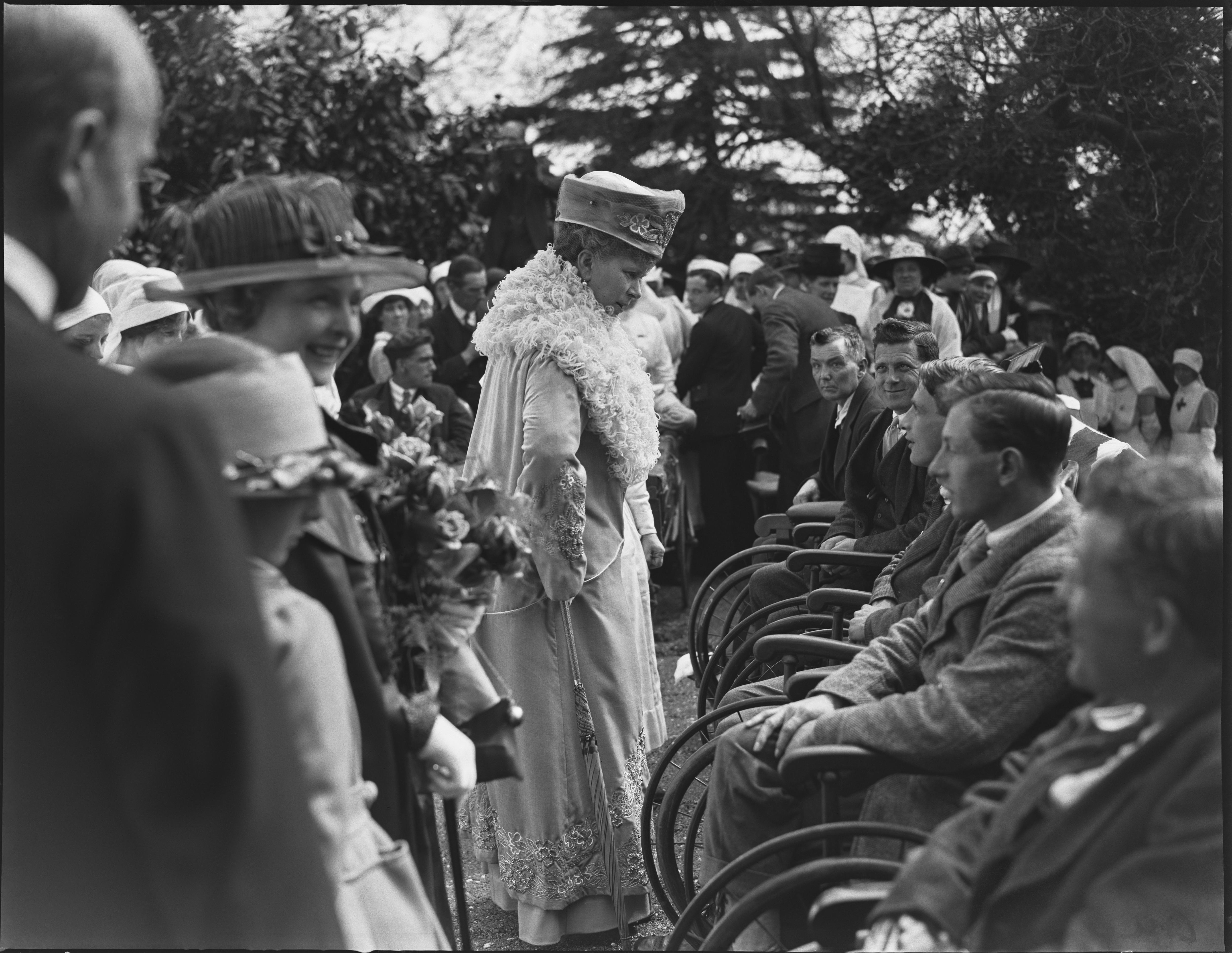 A woman in a frilly scarf and hat talks to men in wheelchairs 