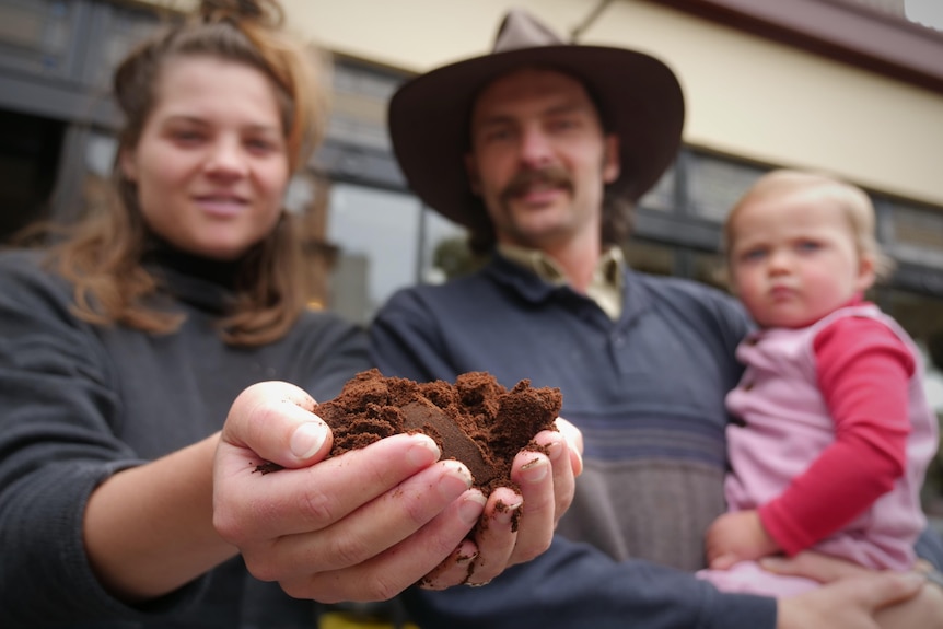 A woman holding handfuls of coffee grounds standing next to a man with a baby.