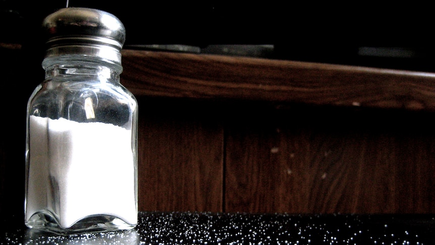 A salt shaker and bits of salt all over a table