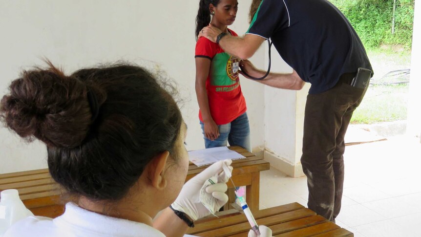 Dr Josh Francis listens to the heart of a patient while a nurse prepares a penicillin injection.