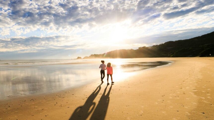 Two people walk on the sand at Byron Bay's Clarkes Beach.