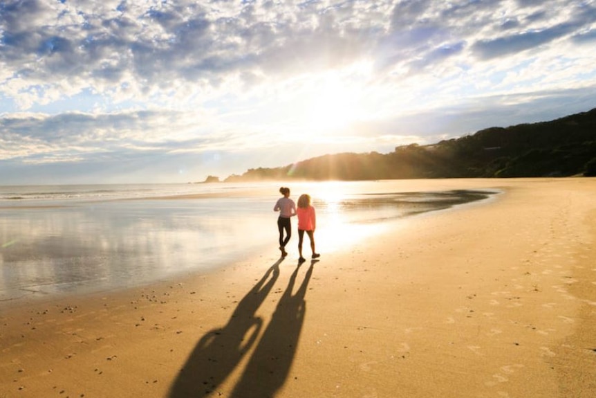 Two people walk on the sand at Byron Bay's Clarkes Beach.