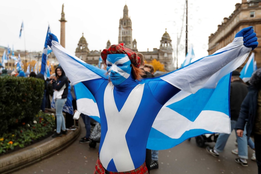 A man dressed in a Scottish mask and wearing a Scottish flag and wig poses.