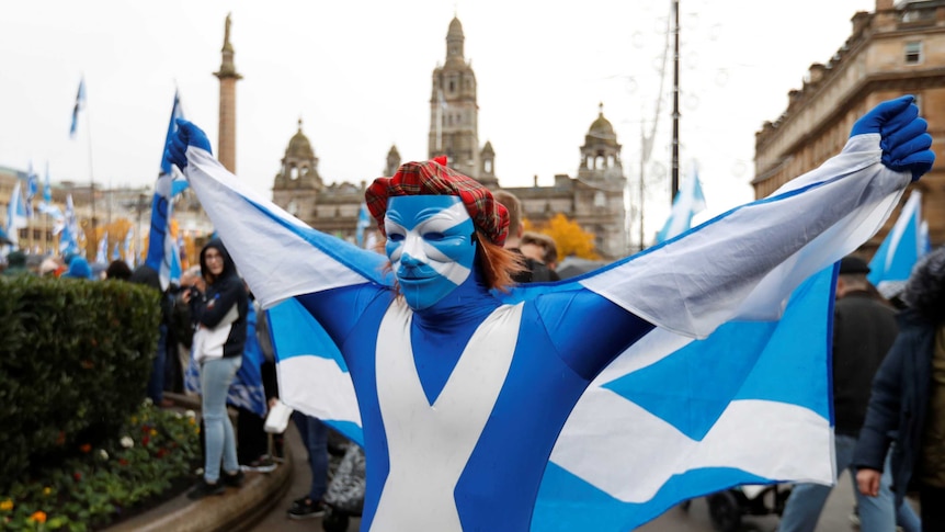 A man dressed in a Scottish mask and wearing a Scottish flag and wig poses.